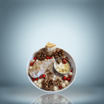A decorative arrangement featuring a quartz crystal cluster, pinecones, red and white decorative balls, a small log piece, a candle with herbs and stones inside, and small dried flowers or seeds