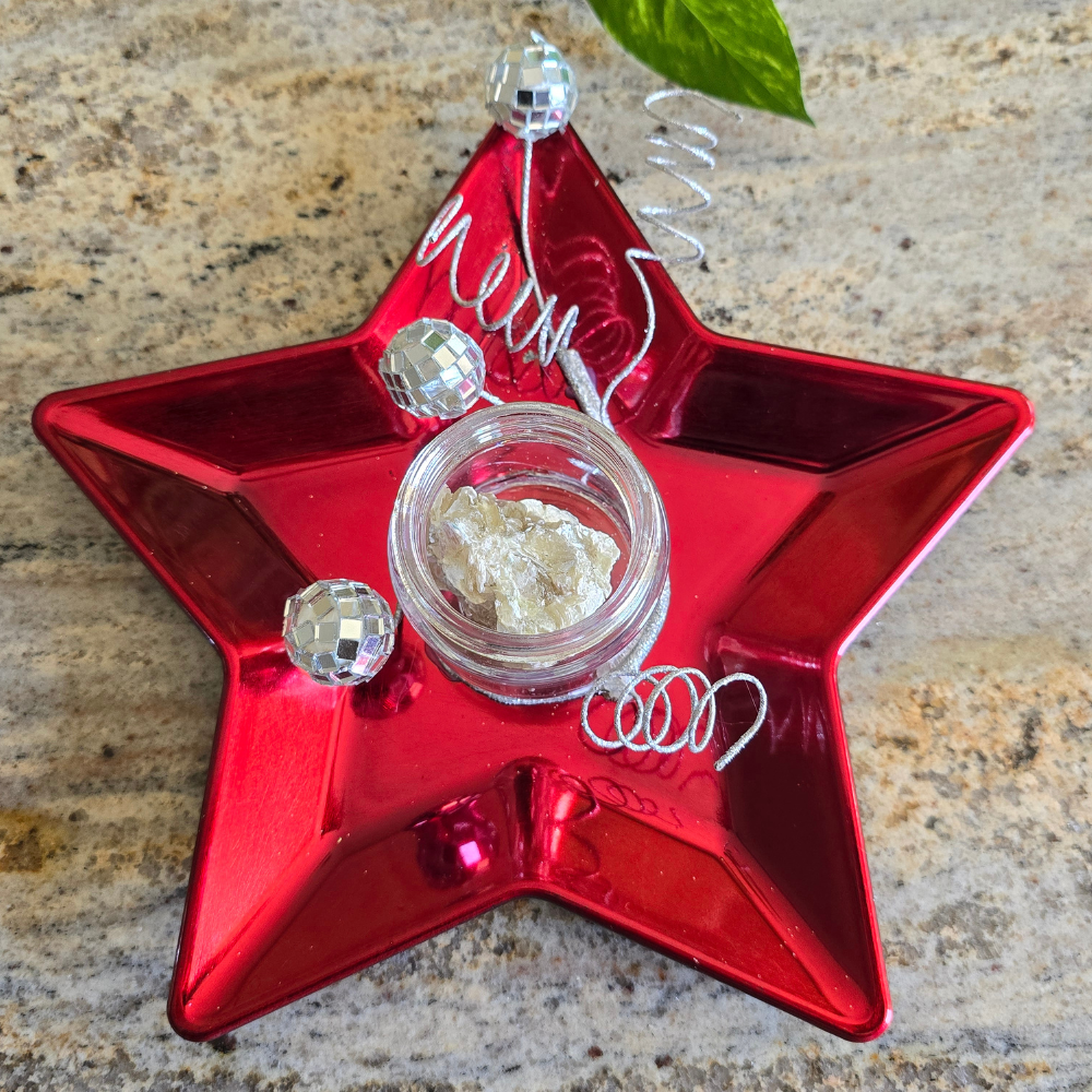 A decorative red star-shaped ornament with a small container of muscovite in the center, adorned with clear beads and silver wire spirals