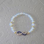 Translucent opalescent bead bracelet with small gold spacer beads and an infinity symbol charm, half encrusted with rhinestones and half dark blue