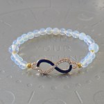 Translucent opalescent bead bracelet with small gold spacer beads and an infinity symbol charm, half encrusted with rhinestones and half dark blue