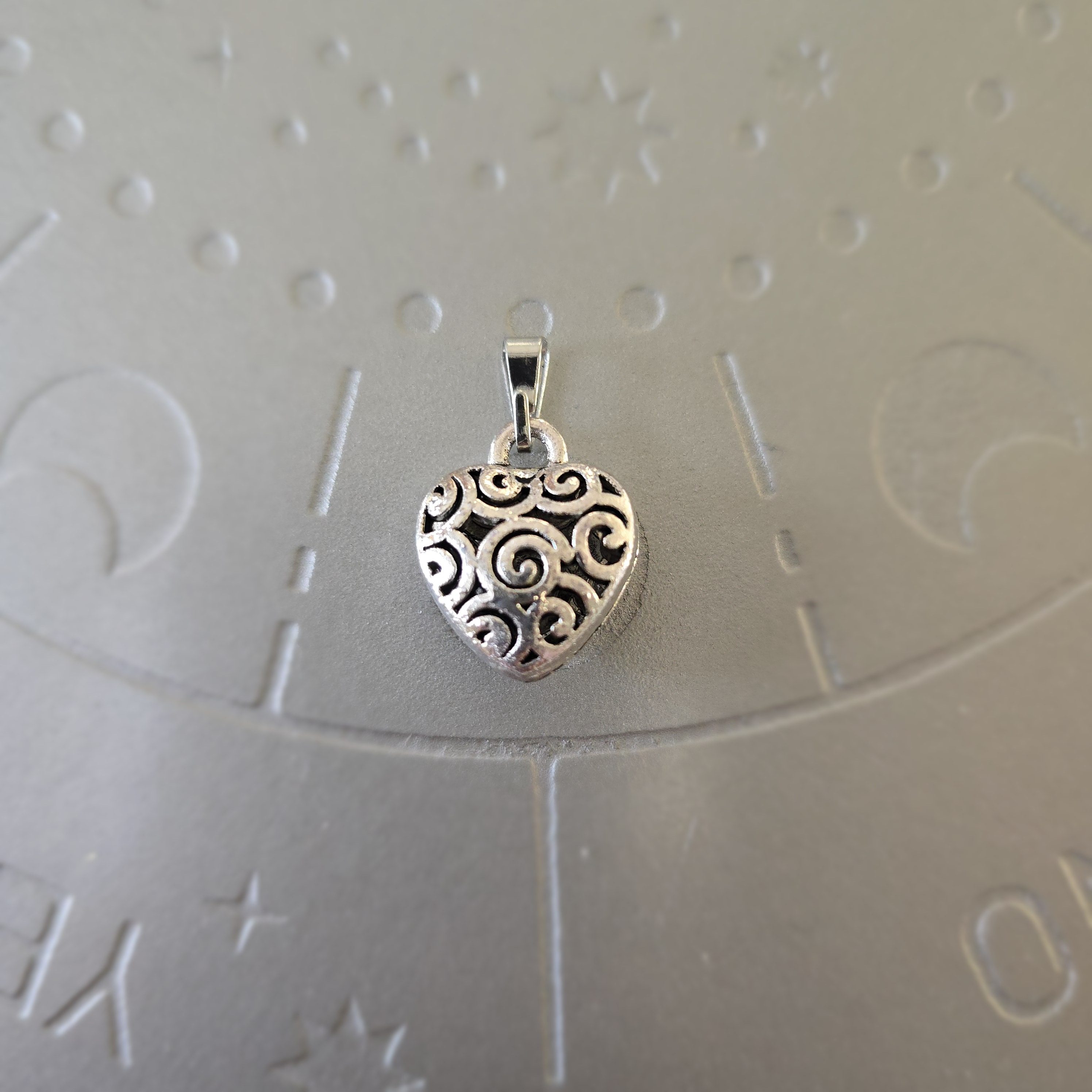 Silver-toned brass heart pendant with intricate swirl design, 1 inch.