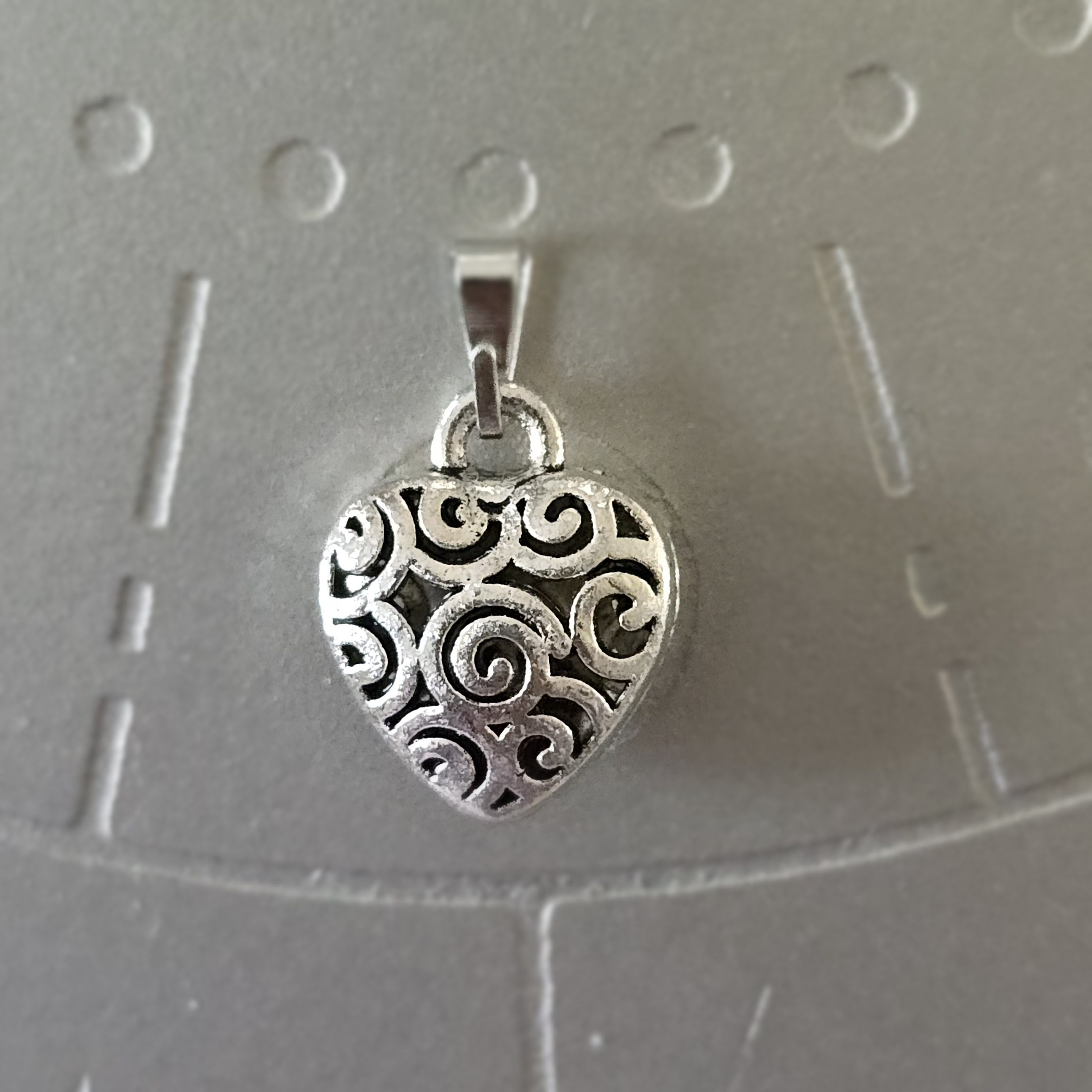Silver-toned brass heart pendant with intricate swirl design, 1 inch.