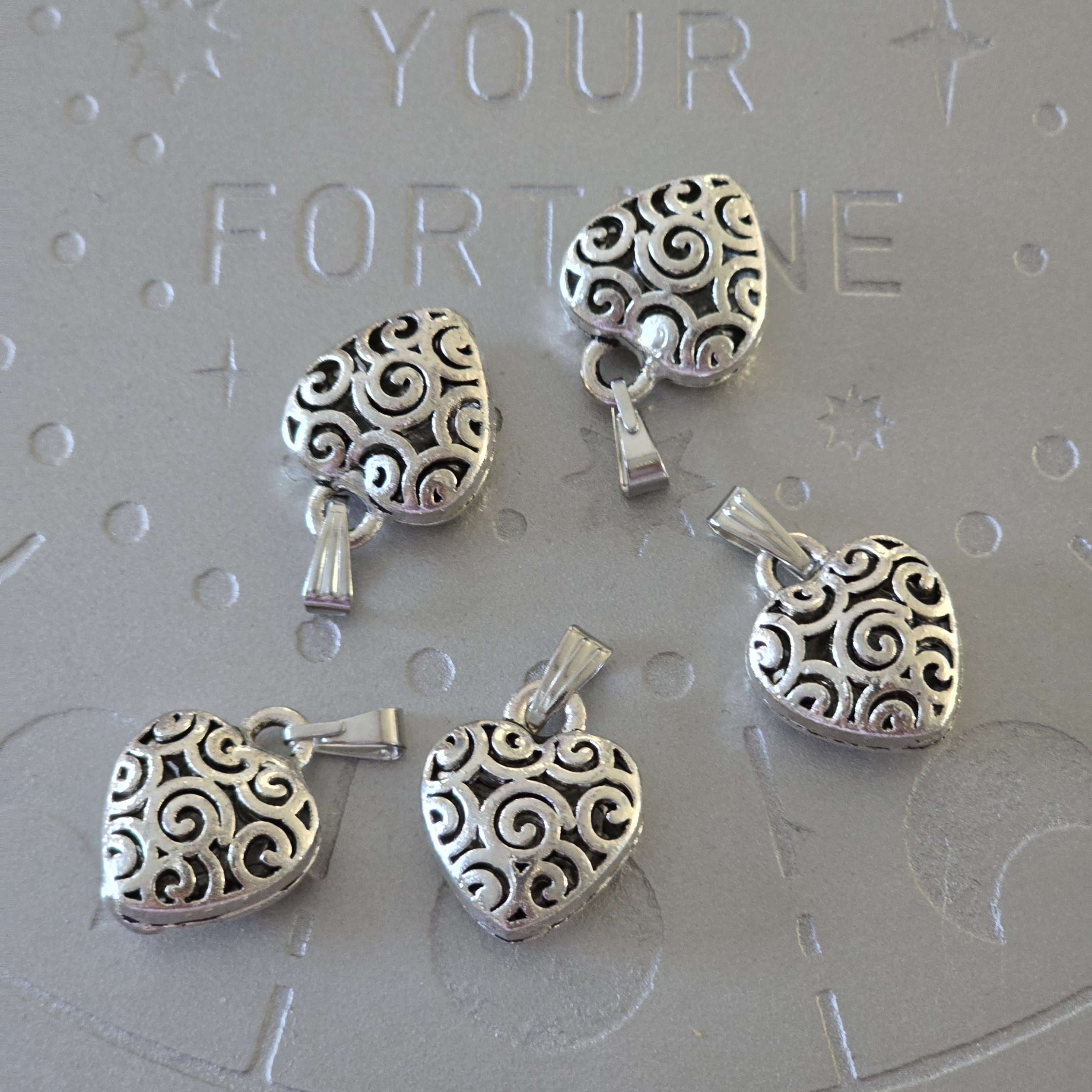 Silver-toned brass heart pendant with intricate swirl design, 1 inch.