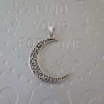 A brass crescent moon pendant with intricate filigree designs, measuring 2 inches in size.