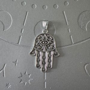 A silver-finished brass pendant shaped like the Hamsa hand, with intricate filigree designs, measuring 2 inches in size.