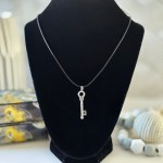 A silver key-shaped pendant hanging from a thin black cord, displayed on a black necklace stand.
