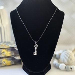 A key-shaped pendant hanging from a thin black cord, displayed on a black necklace stand.