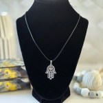 A silver-finished Hamsa hand pendant with intricate filigree designs, featured on an elegant necklace.