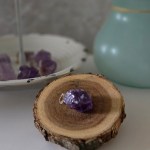 A rough amethyst pendant with a silver bail, displayed on a piece of wood