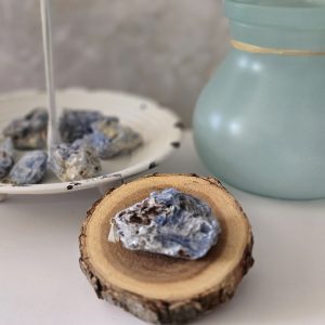 A rough blue kyanite pendant with a sturdy bail displayed on a wood and more stones in the background