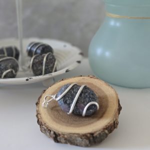 A rough purple garnet pendant displayed on a piece of wood.