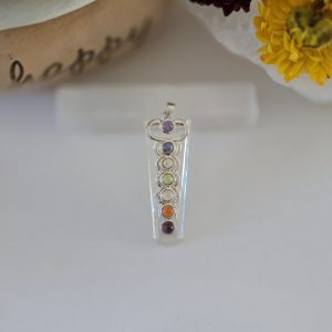 A stunning clear quartz chakra pendulum pendant displayed on a piece of natural selenite stick.
