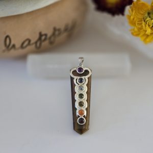 A stunning tiger eye chakra pendant displayed on a piece of natural selenite stick.