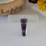 A stunning amethyst chakra pendant displayed on a piece of natural selenite stick.
