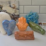 Various shaped bath fizz bombs, with a blue sponge on a white tiled surface.