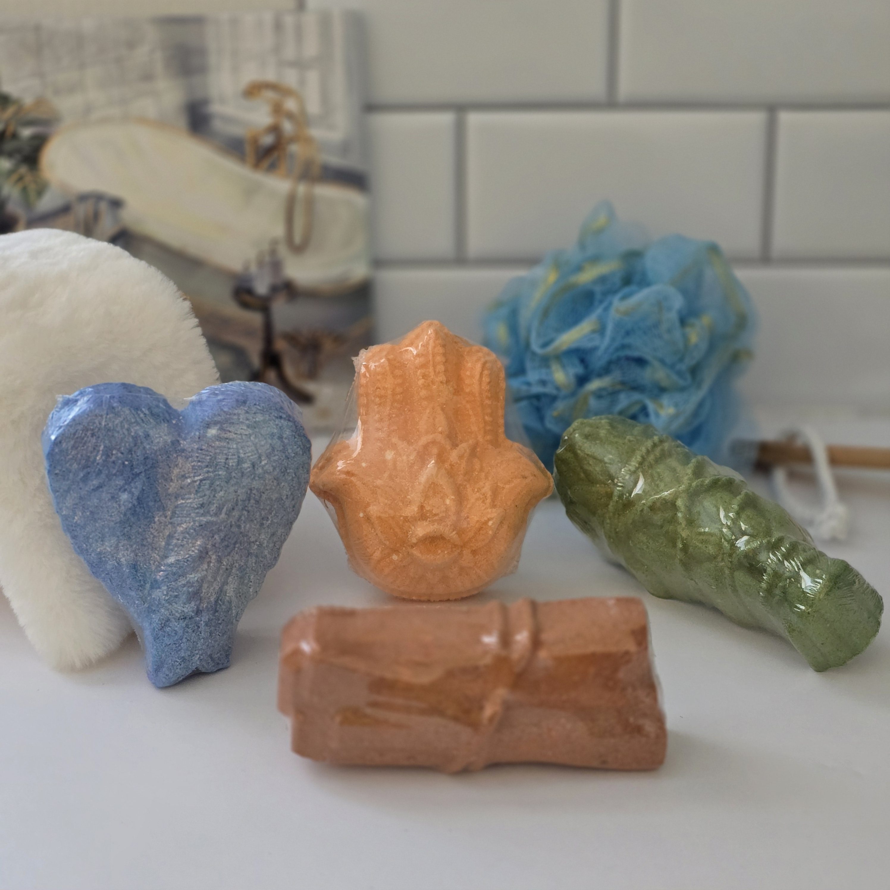 Various shaped bath fizz bombs, with a blue sponge on a white tiled surface.
