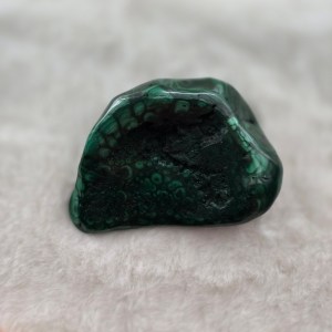 Close-up of a polished Malachite stone with swirling, vibrant green patterns.
