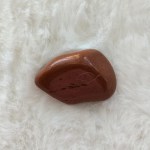 Close-up of a single Red Jasper tumbled stone, showcasing its rich, warm red color and smooth polished surface.