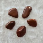 A collection of polished Red Jasper tumbled stones, radiating deep red hues with earthy undertones.