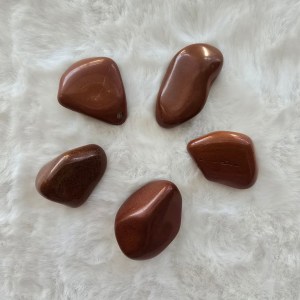 A collection of polished Red Jasper tumbled stones, radiating deep red hues with earthy undertones.